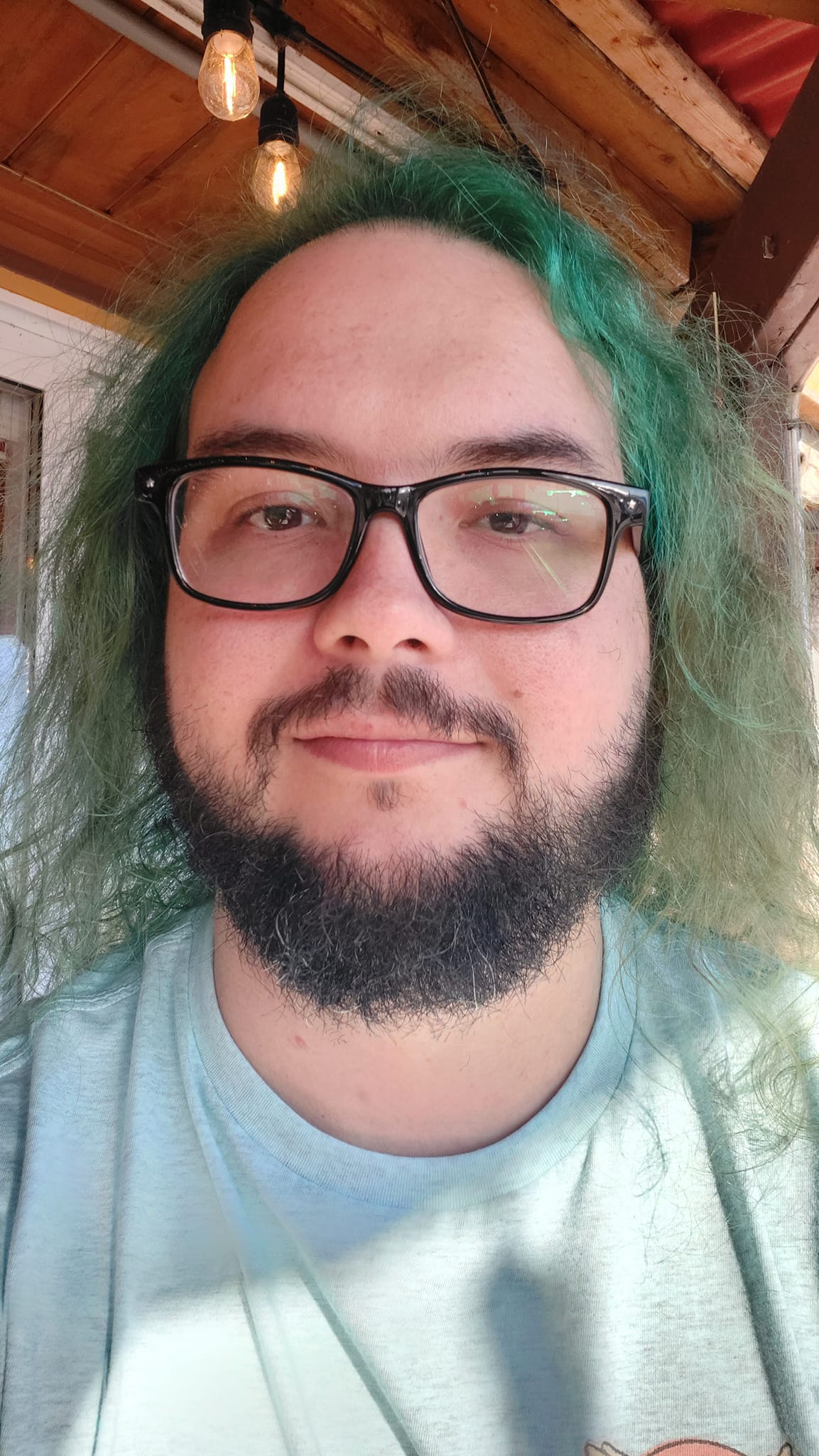 A man with green hair is sitting on a patio in the sunlight, Photo 2